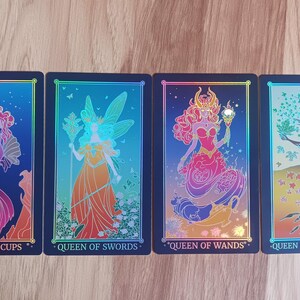 May include: Four tarot cards featuring colorful illustrations of female figures. The cards are labeled "Queen of Cups," "Queen of Swords," "Queen of Wands," and "Queen of Pentacles." Each card has a black border and a holographic effect.