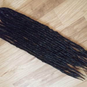 May include: A set of black synthetic dreadlocks, also known as faux locs, for hair extensions. The dreadlocks are long and straight, with a smooth texture.