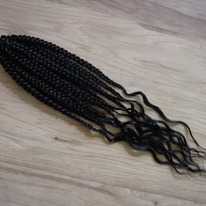 May include: A bundle of black pre-braided hair extensions. The hair is long and wavy.