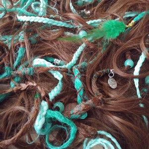 Könnte beinhalten: Nahaufnahme eines Stapels von türkisfarbenen und braunen Haarverlängerungen mit Perlen und Charms. Die Extensions bestehen aus synthetischem Haar und sind dazu bestimmt, dem natürlichen Haar Länge und Volumen zu verleihen.