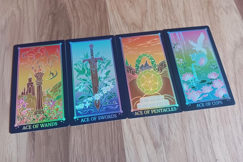 May include: Four tarot cards are displayed, each with a black border and vibrant holographic artwork. The cards are labeled "Ace of Wands," "Ace of Swords," "Ace of Pentacles," and "Ace of Cups," featuring symbolic imagery.