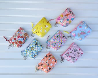May include: Seven small zippered pouches with various colorful patterns and designs. The pouches are made of fabric and have a zipper closure. The pouches are all different sizes and shapes. Some of the pouches have a key chain attached to them.