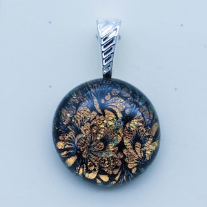 May include: A round glass pendant with a black and gold pattern. The pendant is attached to a silver chain.