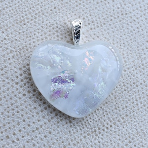 May include: A heart-shaped pendant with a silver bail. The pendant is filled with a white, translucent material with iridescent accents of purple, blue, and silver. The bail is a simple, rectangular design.