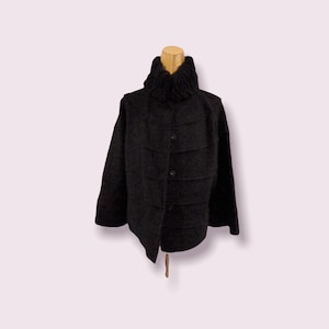 May include: A black knitted jacket with a high collar and button closure. The jacket has a slightly cropped length and a relaxed fit.