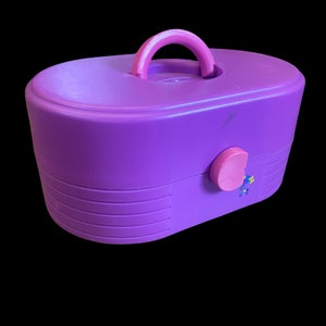 Könnte beinhalten: Eine violette Plastik-Kosmetikbox mit einem rosa Griff und einem rosa Verschluss. Die Box hat ein weiß-violettes Ombre-Design auf der Oberseite.