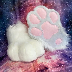 May include: A pair of white furry paws with pink paw pads. The paws are on a purple and pink galaxy print background.
