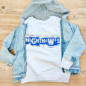 May include: White sweatshirt with a blue graphic that says "boyden-hull rock valley NIGHTHAWKS". The sweatshirt is layered over a denim jacket with a gray hooded sweatshirt underneath.