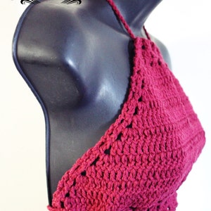 May include: A handmade, magenta crochet halter top. The top is displayed on a black mannequin. The top features a halter neck tie and a textured, open stitch design. The text "TEASE ME THREADS" is in a decorative font.