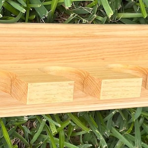 May include: A light-colored wooden shelf with a series of evenly spaced, rectangular cutouts. The shelf is rectangular with a slightly raised front edge and a decorative end. The shelf is made of natural wood.