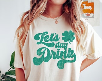 Może przedstawiać: Biała koszulka z zieloną koniczyną i napisem "Let's day Drink" w retro czcionce.
