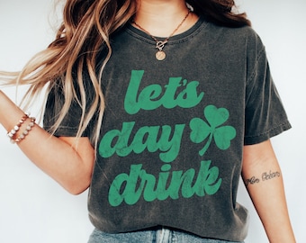 Może przedstawiać: Modelka nosi szary t-shirt z zieloną koniczyną i napisem "let's day drink". Modelka nosi niebieskie dżinsy i białe buty sportowe. Modelka nosi rozmiar S.