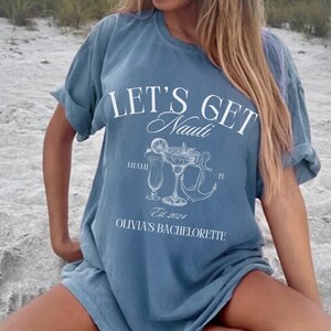May include: Blue jean-coloured t-shirt with the text "LET'S GET Nauti" in white script. Below the text are illustrations of cocktails, an anchor, and the words "Miami FL" and "Olivia's Bachelorette Est. 2024". The shirt is size L.