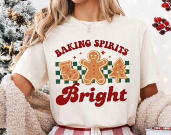 May include: A white t-shirt with the text "Baking Spirits Bright" in red and black lettering. The design features a gingerbread man, a stocking, and a Christmas tree.