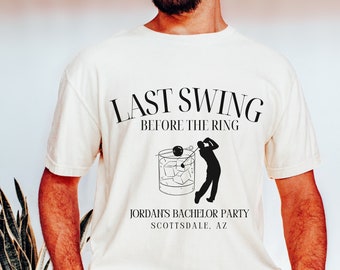 以下が含まれることがあります： アイボリー色のTシャツに、黒い文字で「Last Swing Before The Ring」と、氷を入れたグラスにクラブを振るっているゴルファーのグラフィックがプリントされています。グラフィックの下には「Jordan's Bachelor Party Scottsdale, AZ」という文字が書かれています。