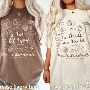 Op de afbeelding: Twee T-shirts met een thema voor een vrijgezellenfeest. Het linker T-shirt is bruin met ivoor kleurige tekst die zegt "a tini bit tipsy" en "Olivia's Bachelorette Scottsdale, AZ". Het rechter T-shirt is ivoor met bruine tekst die zegt "a Bride in a tini bit" en "Olivia's Bachelorette Scottsdale, AZ".