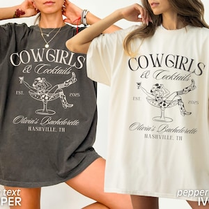 May include: Two oversized t-shirts featuring a graphic design of a cowgirl in a martini glass. The text on the shirts reads "Cowgirls & Cocktails" and "Olivia's Bachelorette Nashville, TN". One shirt is black with ivory text and the other is ivory with black text.