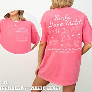 May include: A pink t-shirt with white text that says "Girls Gone Mild" and includes a design of wine glasses, a sleep mask, and other hen party themed items. The text also says "Oakleigh's Bachelorette Knoxville, TN".