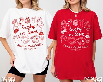 May include: Two oversized t-shirts, one white and one red, feature a playful design with the text "lucky in love" and Las Vegas-themed illustrations. The shirts also include the text "Olivia's Bachelorette" and the location.