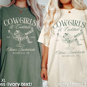 May include: Two oversized t-shirts featuring a cowgirl in a martini glass design. The text on the shirts reads "Cowgirls & Cocktails" with the years "EST. 2025". One shirt is moss green with ivory text and the other is ivory with moss green text. Both shirts say "Olivia's Bachelorette Nashville, TN".