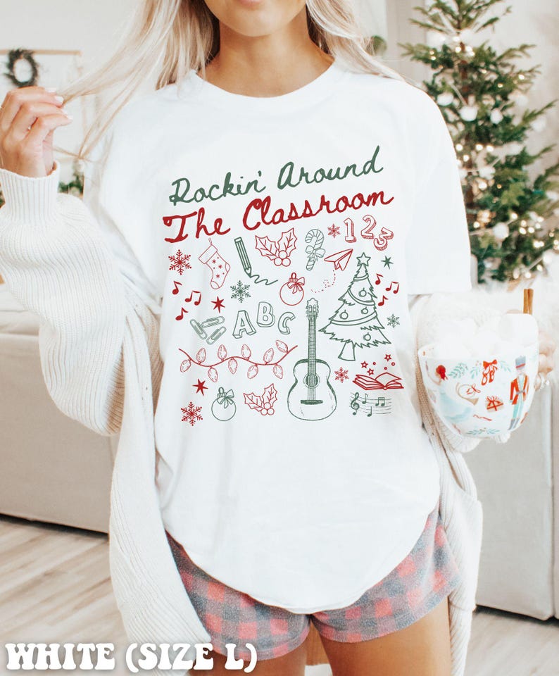 May include: White t-shirt with the text "Rockin' Around The Classroom" and a variety of Christmas-themed illustrations, including a Christmas tree, a guitar, a stocking, a candy cane, a pencil, and a book.