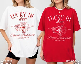 May include: Two oversized t-shirts, one white and one red, each featuring a graphic design. The design includes the text "LUCKY IN love", a martini glass, playing cards, dice, and the text "Kenzie's Bachelorette, Las Vegas, NV."