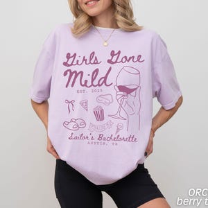 May include: Purple t-shirt with the text "Girls Gone Mild Est. 2025" and a graphic of a wine glass, a pizza slice, popcorn, a cupcake, and flip flops. The text "Sailor's Bachelorette Austin, TX" is below the graphic.