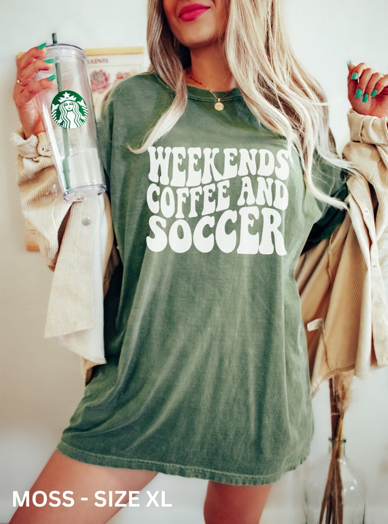 May include: A moss green oversized t-shirt with the text "Weekends Coffee and Soccer" in white retro font.