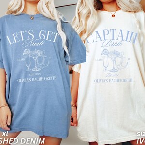 May include: Two oversized t-shirts, one in washed denim blue and the other ivory, with a bachelorette party theme. The blue shirt reads "LET'S GET Nauti" with a cocktail and anchor graphic. The ivory shirt says "CAPTAIN Bride" with a similar design. Both shirts have "Olivia's Bachelorette" and "Est. 2024".