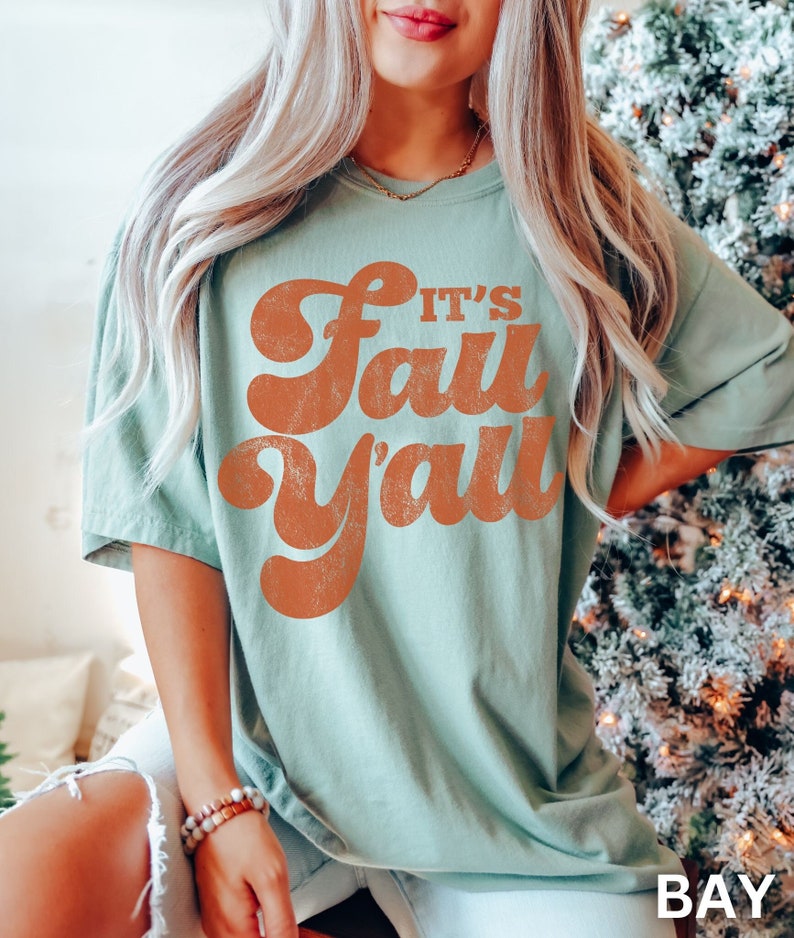 May include: A light green t-shirt with a retro-style orange graphic that says "It's Fall Y'all".