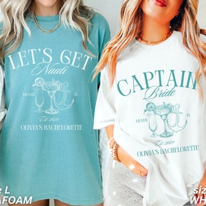 May include: Two oversized t-shirts, one seafoam and one white, with matching graphic designs. The seafoam shirt reads "LET'S GET Nauti" with a cocktail and anchor illustration. The white shirt says "CAPTAIN Bride" with a similar design. Both shirts say "Miami, FL" and "Olivia's Bachelorette".