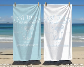 May include: Two beach towels with the text "Last Toast on the Coast" in white on a blue background and a white background. The towels are hanging on a clothesline against a beach background.