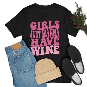 Peut inclure: T-shirt noir avec un motif rose et blanc qui dit "Girls Just Wanna Have Wine" dans une police r&eacute;tro.