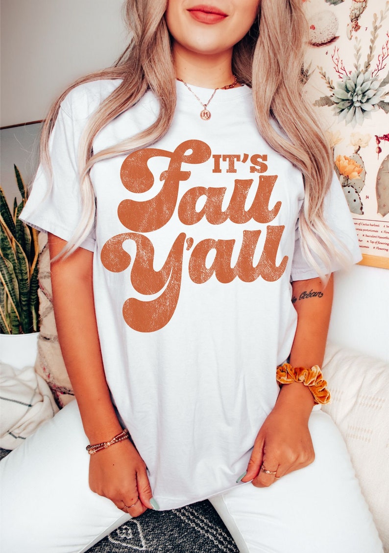 May include: White t-shirt with a brown graphic that says "It's Fall Y'all" in a retro font.