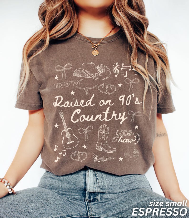 May include: Espresso-colored t-shirt with the text "Raised on 90's Country" and country-themed graphics. The design includes a cowboy hat, guitar, boots, musical notes, and the word "Howdy". The shirt is size small.