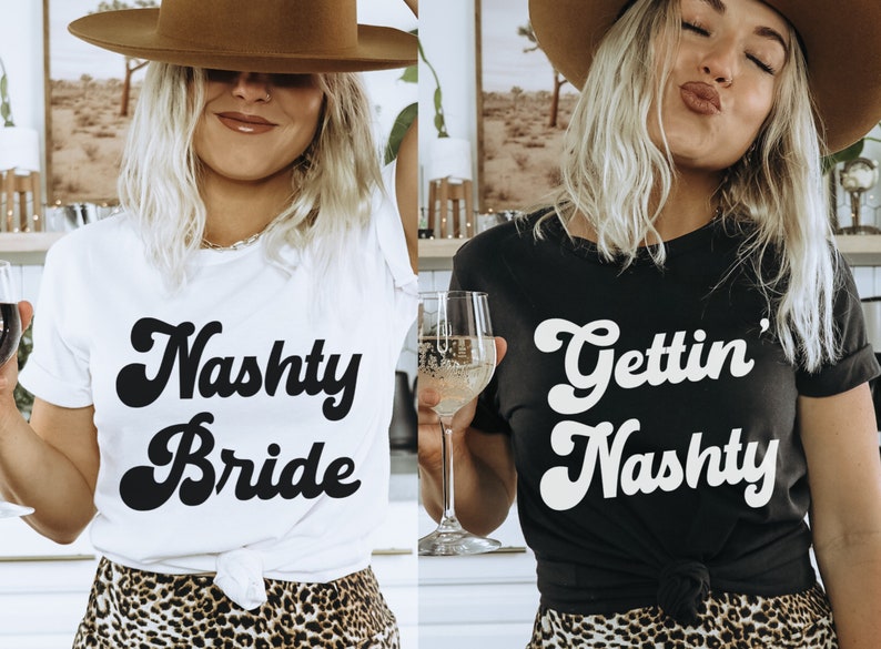 Pu&ograve; includere: Due donne indossano magliette bianche e nere con il testo "Naughty Bride" e "Gettin' Naughty" in un font retr&ograve;. Entrambe le donne indossano cappelli da cowboy marroni e gonne a stampa leopardata.