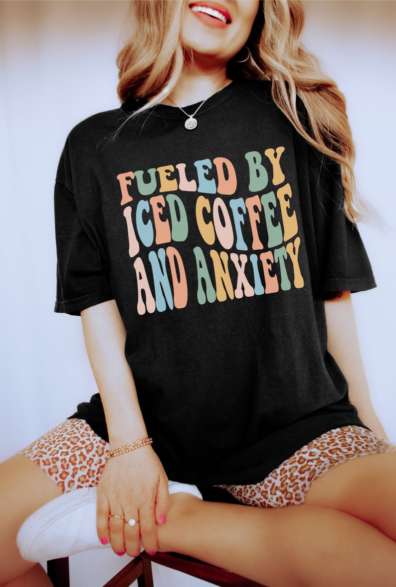 Peut inclure: T-shirt noir avec l'inscription "FUELED BY ICED COFFEE AND ANXIETY" dans un style r&eacute;tro color&eacute;. Le t-shirt a une coupe ample, parfaite pour un look d&eacute;contract&eacute;. L'ensemble d&eacute;gage une ambiance vintage et amusante.