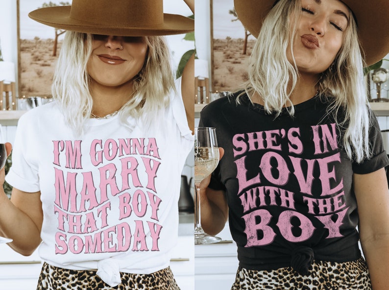 Puede incluir: Dos mujeres con camisetas con texto rosa. La camiseta blanca dice "Voy a casarme con ese chico alg&uacute;n d&iacute;a". La camiseta negra dice "Ella est&aacute; enamorada del chico".