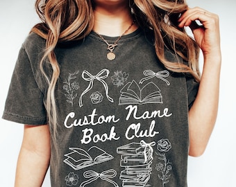 Peut inclure: Un t-shirt gris foncé avec un motif blanc représentant des livres, des nœuds et le texte "Custom Name Book Club".