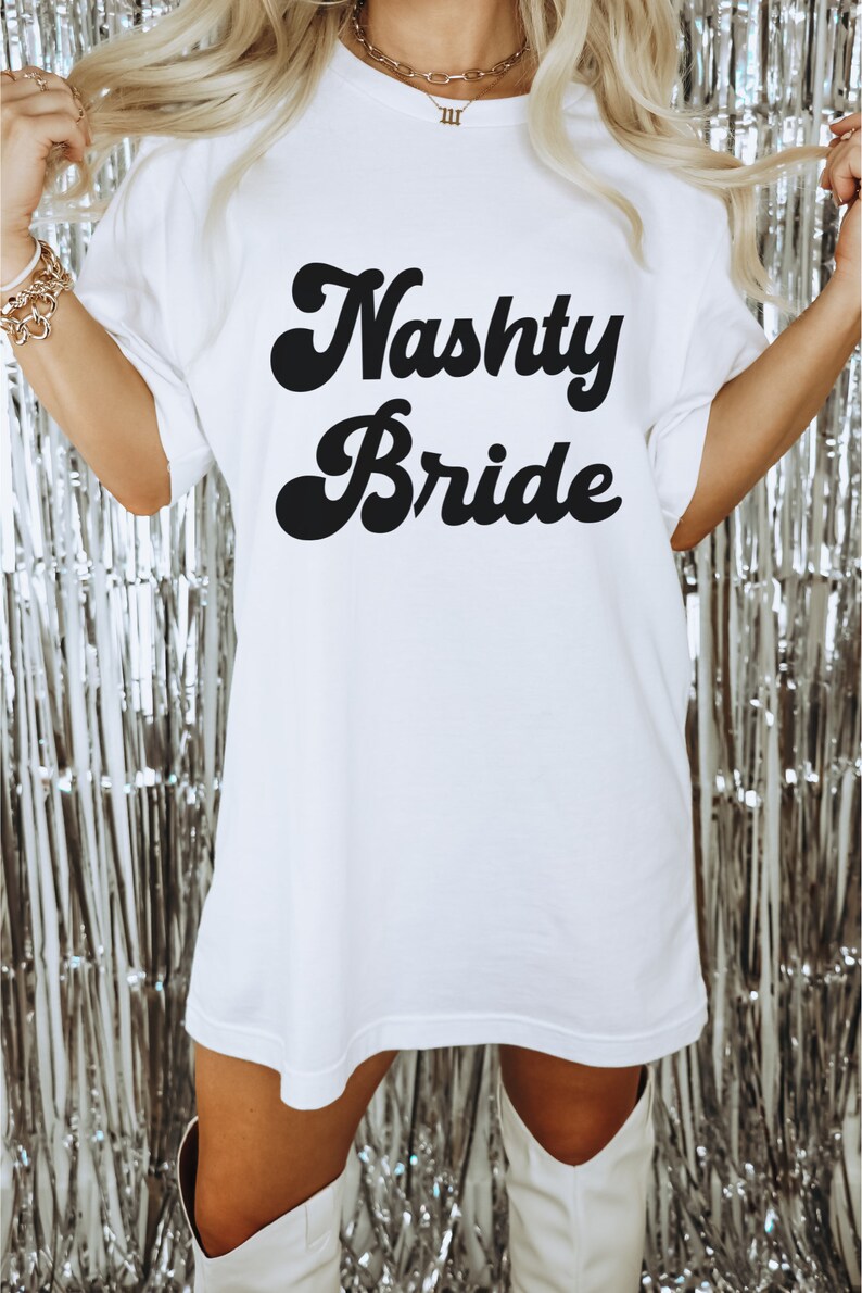 Pu&ograve; includere: Maglietta bianca oversize con testo nero che recita "Nasty Bride" in un font retr&ograve;.