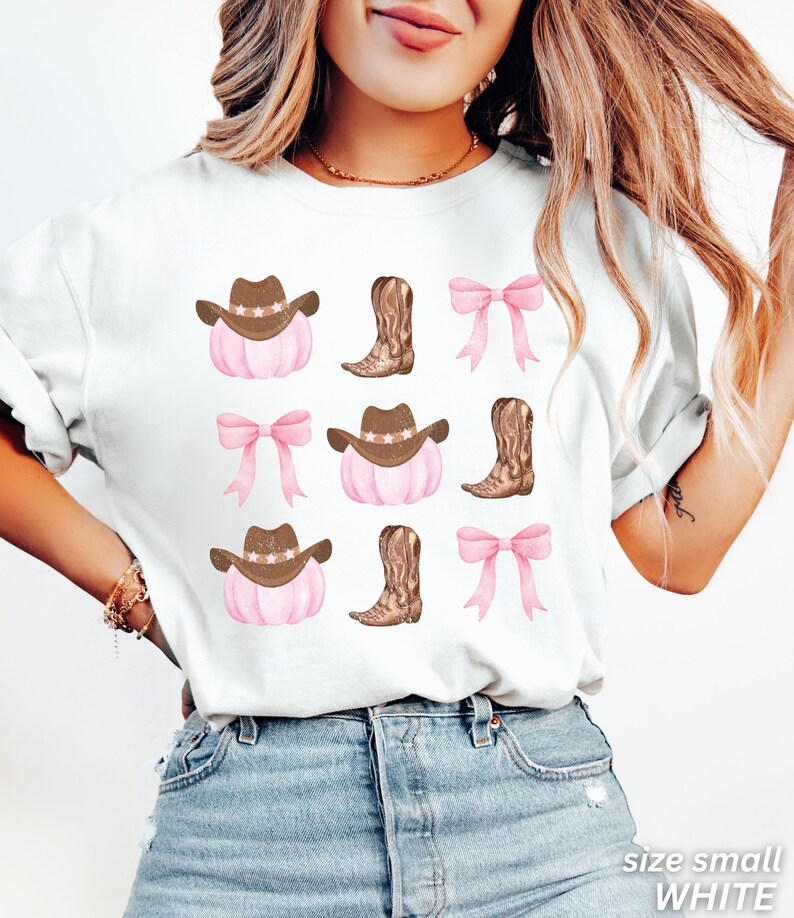 May include: White t-shirt with a repeating pattern of cowboy hats, boots, and bows. The cowboy hats have star accents, and the boots are brown. The bows are pink. The text "size small WHITE" is at the bottom right.