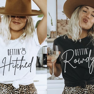 Puede incluir: Dos mujeres con camisetas blancas y negras con el texto "Gettin' Hitched" y "Gettin' Rowdy" en escritura negra. Ambas mujeres llevan sombreros marrones y faldas de estampado de leopardo.