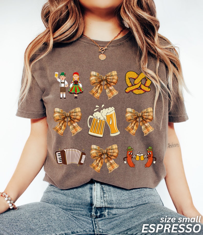 Op de afbeelding: Een bruin T-shirt met een feestelijk Oktoberfest-thema. Het ontwerp bevat een stel in traditionele Duitse kleding, pretzels, bierkruiken, accordeons en strikken met ruitjespatronen.
