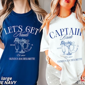 May include: Two t-shirts, one navy blue and one white, with nautical designs. The navy shirt has the text "LET'S GET Nauti" with a cocktail, anchor, and text "Miami, FL, Est. 2024, Olivia's Bachelorette." The white shirt says "CAPTAIN Bride" with similar graphics and text.