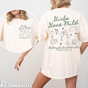 May include: A white t-shirt with a green graphic that says "Girls Gone Mild" and includes illustrations of wine glasses, a sleep mask, and other party favours. The text "Oakleigh's Bachelorette Knoxville, TN" is also included on the shirt.