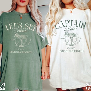 May include: Two oversized t-shirts, one moss green and one ivory, with nautical designs. The green shirt reads "Let's Get Nauti", the ivory shirt says "Captain Bride". Both have cocktail and anchor illustrations, with "Olivia's Bachelorette" and "Est. 2024".