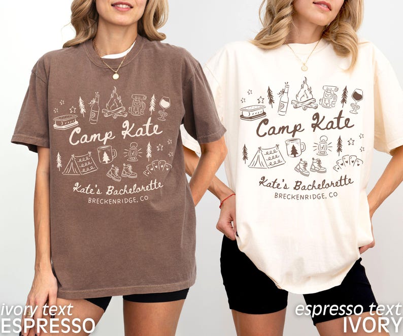 May include: Two short-sleeved t-shirts, one brown and one ivory, each with a white graphic. The graphic includes the text "Camp Kate" and "Kate's Bachelorette, Breckenridge, CO" along with camping-themed illustrations like a tent, campfire, and hiking boots.
