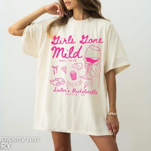 May include: Ivory t-shirt with pink text that reads "Girls Gone Mild Est. 2023 Sailor's Bachelorette Austin, TX". The shirt features a pink illustration of a glass of wine, pizza, popcorn, and flip flops.