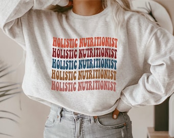 May include: A grey sweatshirt with the text "HOLISTIC NUTRITIONIST" repeated five times in a rainbow colour pattern. The text is in a retro font style.