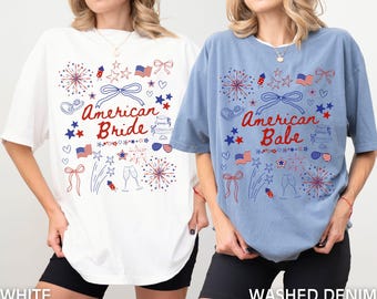 Könnte beinhalten: Zwei T-Shirts mit einem 4. Juli-Thema. Eines ist weiß mit dem Text "American Bride" und das andere ist blau mit dem Text "American Babe". Beide Shirts zeigen rote, weiße und blaue Sterne, Feuerwerk und andere patriotische Bilder.
